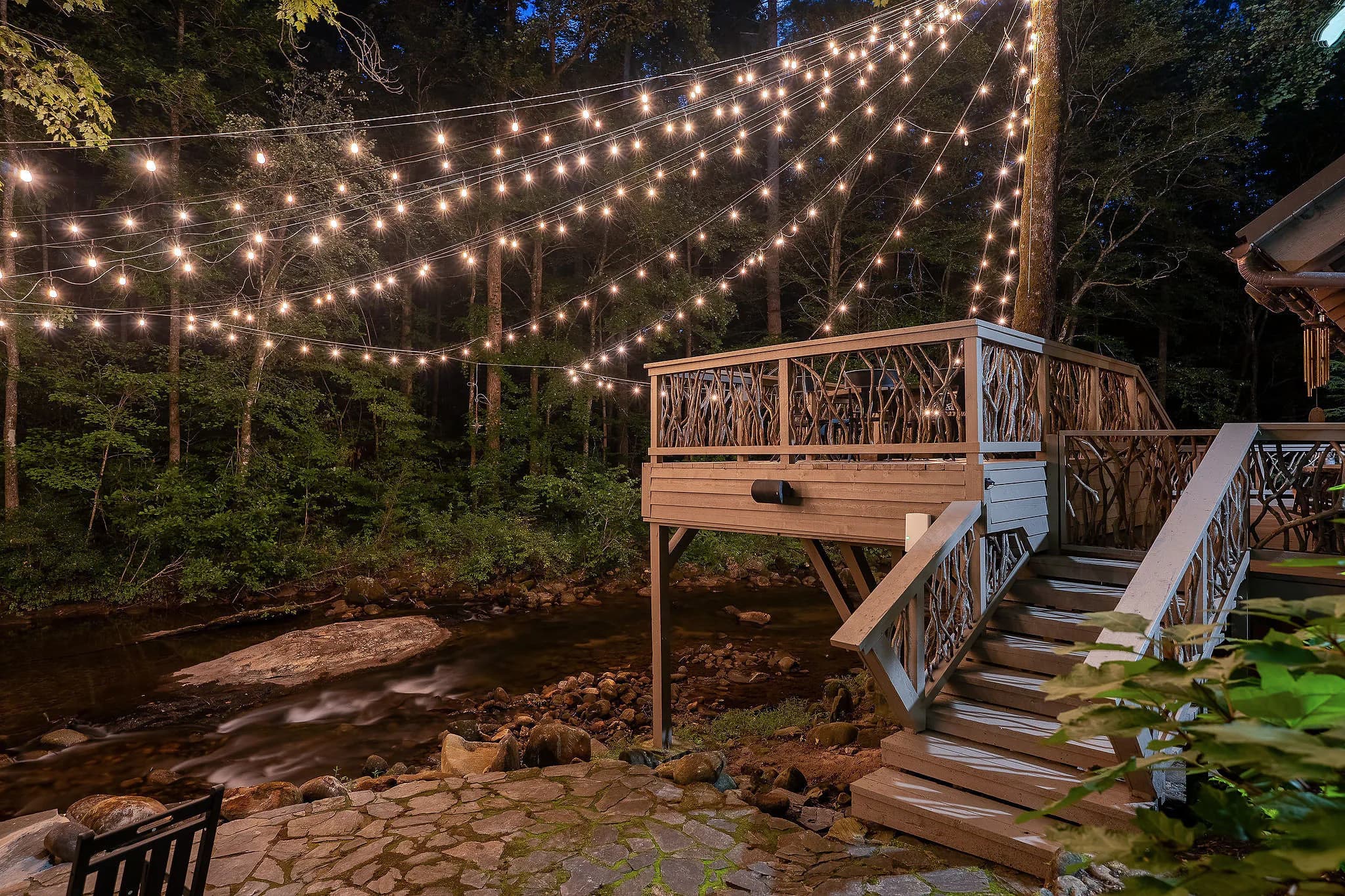 Deck and branch railing stairs over the Middle Saluda River under string lights at a riverfront cabin in Marietta SC